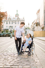 Obraz premium Young Couple In Wheelchair Strolling In old City. Lovely couple, woman in wheelchair and her husband, walking outdoors in the city