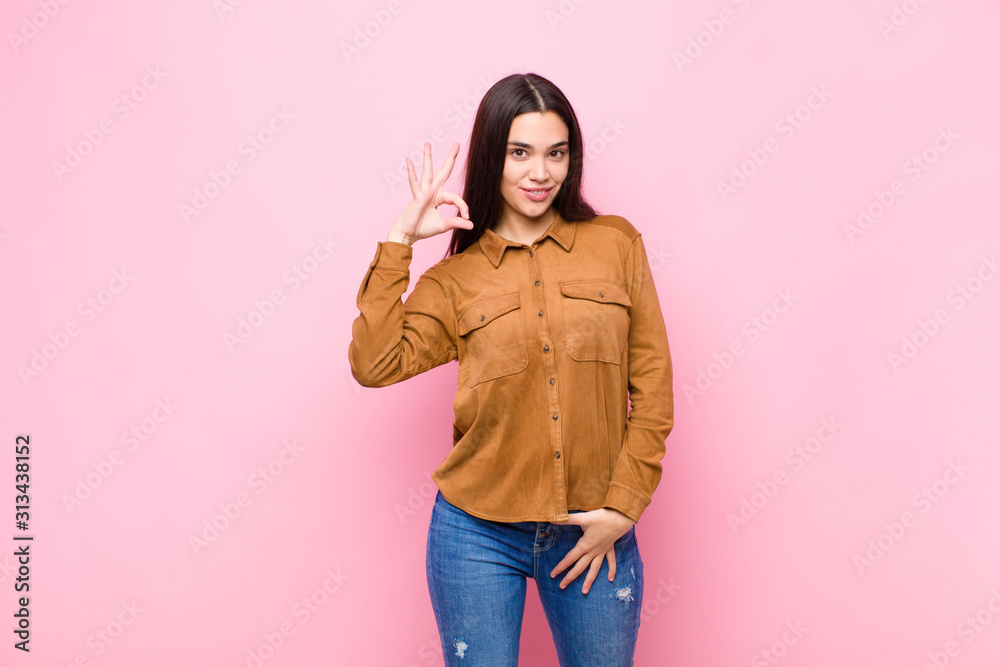 Wall mural young pretty woman feeling successful and satisfied, smiling with mouth wide open, making okay sign 