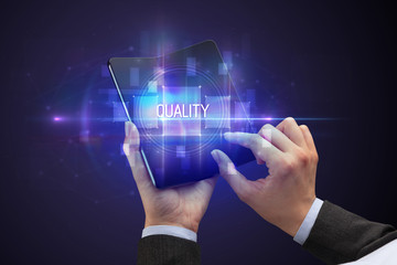 Businessman holding a foldable smartphone with QUALITY inscription, new technology concept