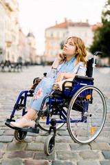 attractive disabled young woman in blue dress sitting in a wheelchair, outdoors in the city