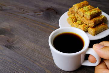 Fingers Holding a Cup of Turkish Coffee with Blurry Plate of Baklava Pastries in the Backdrop