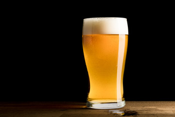 Beer in glass, spilled on wooden table, isolated on black background, copy space