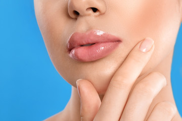 Obraz na płótnie Canvas Young woman with beautiful full lips on light blue background, closeup