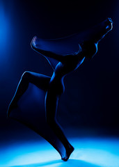 Slim girl wearing a white bodysuit dances a modern avant garde dance, covering her body with elastic transparent fabric in blue light. Artistic, conceptual and creative design. Silhouette photography.