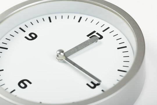 15 minutes after twelve white with light metal minimalistic clock close-up on a light background