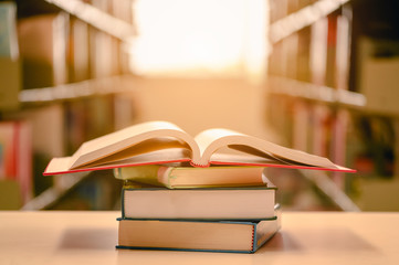 Opened book with stack of books on the desk wood in the library.  Education background concept.