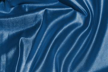 Shining classic blue silk atlas satin fabric with folds, fabric waves. Real fabric background. Color of the year 2020