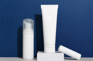 Facial and body care cosmetics bottles composition on classic blue background. Gel tube, lipstick, cream jar unbranded blank packages. Skincare female products advertising with trendy backdrop