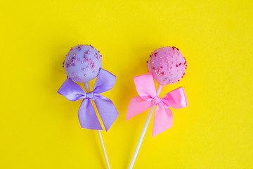 Cake pops with pink and violet bows in the center of  the yellow  background. Top view. Copy space. Closeup.