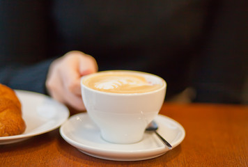 Woman hand holding white cup of cappuccino