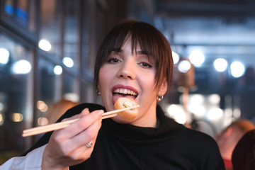 Awesome woman is eating Philadelphia sushi with chopstick close up portrait.