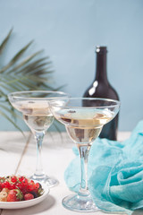 White wine in a glasses, bottle and plate with berries on the white wooden table. Dinner for two.