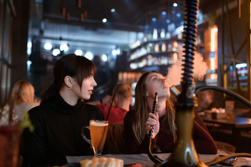 Girlfriends smoking hookah at shisha bar at holidays.