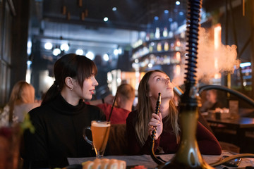 Girlfriends smoking hookah at shisha bar at holidays.
