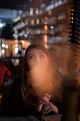 Closeup portrait of a pretty woman sitting in hookah lounge bar and exhale a smoke cloud.