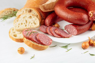On a white wooden table sausage with bread, rosemary, onion and pepper.