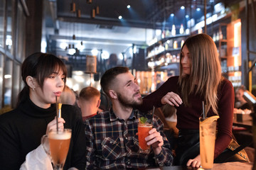 Two pretty women compete because of a man. Happy friends drinking cocktails in the bar. Party at holidays.