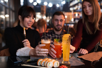 Young hipsters at the cocktail party holding glasses with tasty colourful drinks.