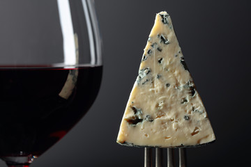 Piece of blue cheese on a fork and red wine.