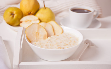Oatmeal porridge with ripe pears in the white bowl, a bowl of pears and cup of coffee on the background. Health breakfast. Close up.