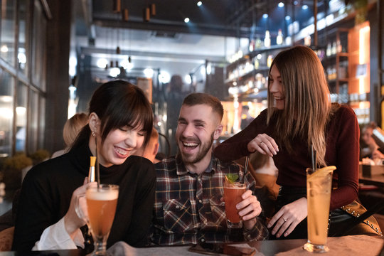 Cheerful smiling young intergender friends laughing. Young people at cocktail party in the lounge bar. Two woman and a man have a dating. - Powered by Adobe