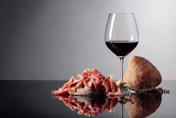 Prosciutto with ciabatta, red wine and thyme on a black background.
