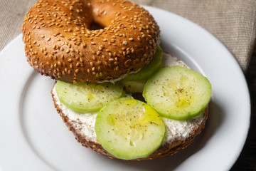 Sesame bagels with spreadable cream cheese and cucumber on wooden background