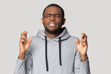 Superstitious african guy closed eyes crossing fingers wishing good luck