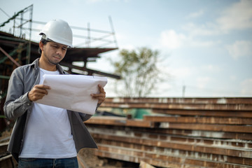 Asian Engineer Man Wearing Safety Helmet and Check Blueprint at Construction Site , Engineer Architect Construction Site Planning Concept