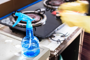 Close up of blue spray bottle with blurred motion woman hand cleaning in kitchen.