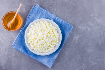 Cottage cheese and honey. Fresh cottage cheese on a gray background. Homemade curd on a blue napkin on cement background. Top view. Copy space