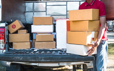 Cropped image of delivery man standing and holding many parcel boxes at his pickup.
