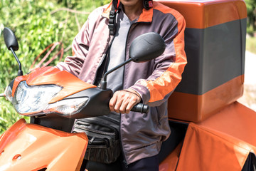 Selective focus at hand of delivery man in orange uniform using motorcycle to delivery parcel.