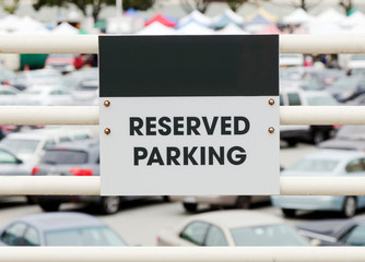 RESERVED PARKING sign on metal railing with parked cars in defocused background. Copy space on area above sign.