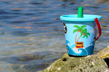 Beach bucket and shovel on the rock beach in Italy with sea in the background - summer holiday...