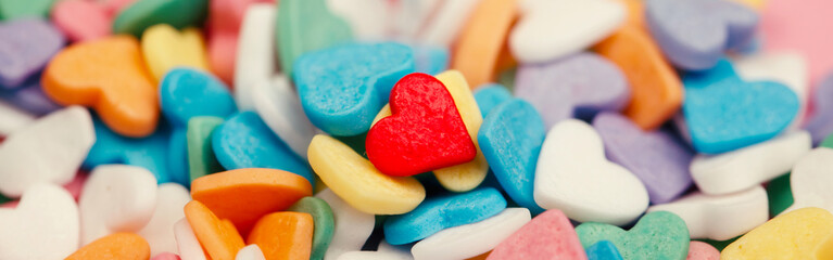 Happy Valentine day. Many small candies colorful hearts. One red heart in centre. Concept of love and February holiday. Web banner header for website. Loneliness in crowd among others.