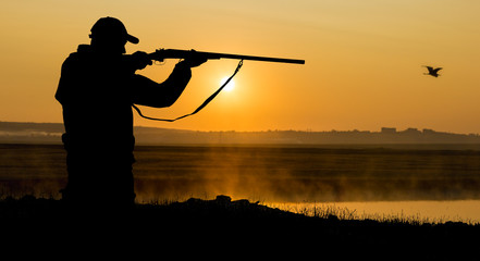 Fototapeta na wymiar Silhouette of a hunter on the background of the morning red dawn. Stands at the ready with a gun.