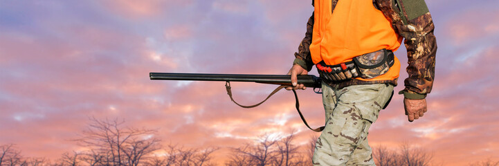 Silhouette of a hunter on the background of the morning red dawn. Stands at the ready with a gun.