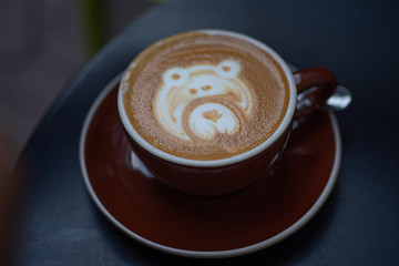 Adorable  bear cappuccino foam art in brown cup on dark blue table.