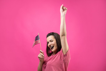 Obraz na płótnie Canvas Happy young woman holding American flag against a studio pink background