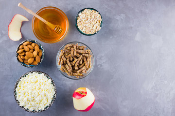 Healthy diet breakfast. Ingredients for a healthy breakfast: oatmeal, granola, honey, almonds, apple, cottage cheese. Homemade granola on a gray background. Top view