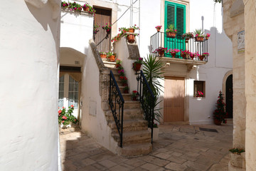 Fototapeta premium Street in Locorotondo town, Italy, region of Apulia, Adriatic Sea - entrance to the houses with stairway and balcony full of flowers