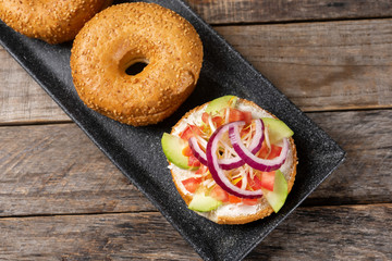 Sesame bagels with spreadable cream cheese and vegetables on wooden background