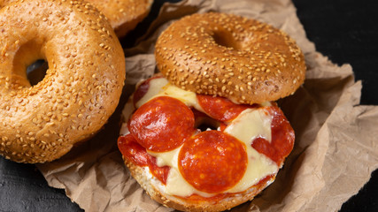 Sesame bagels with pepperoni and cheese on dark background