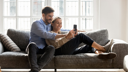 Smiling young couple relaxing at home using modern smartphone