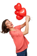 A beautiful brunette Girl with a wide smile in jeans and a pink jacket on a white background holding red balloons in the form of a heart