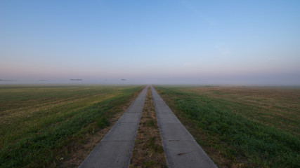 Field path through meadows covered with fog during sunrise