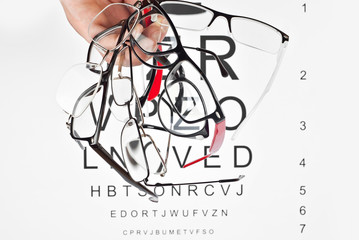 Glasses on a white background. Background with letters for vision test. Many glasses in hand.