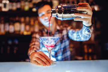 Barman make red alcoholic cocktail with blue smoke in martini glass, decorated with orange