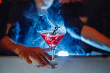 Barman is preparing mix cocktail in shaker of red alcohol and ice glass, bar counter